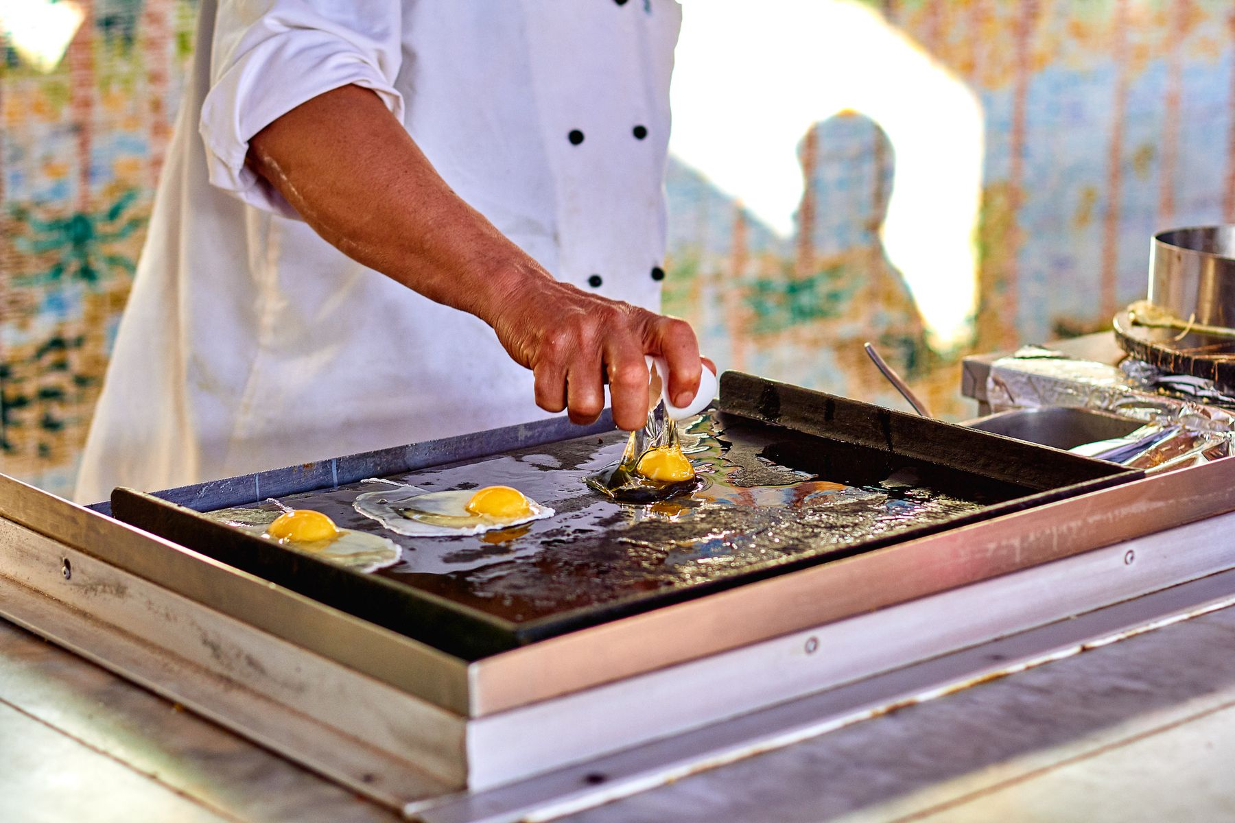 A cook preparing fresh eggs on a griddle