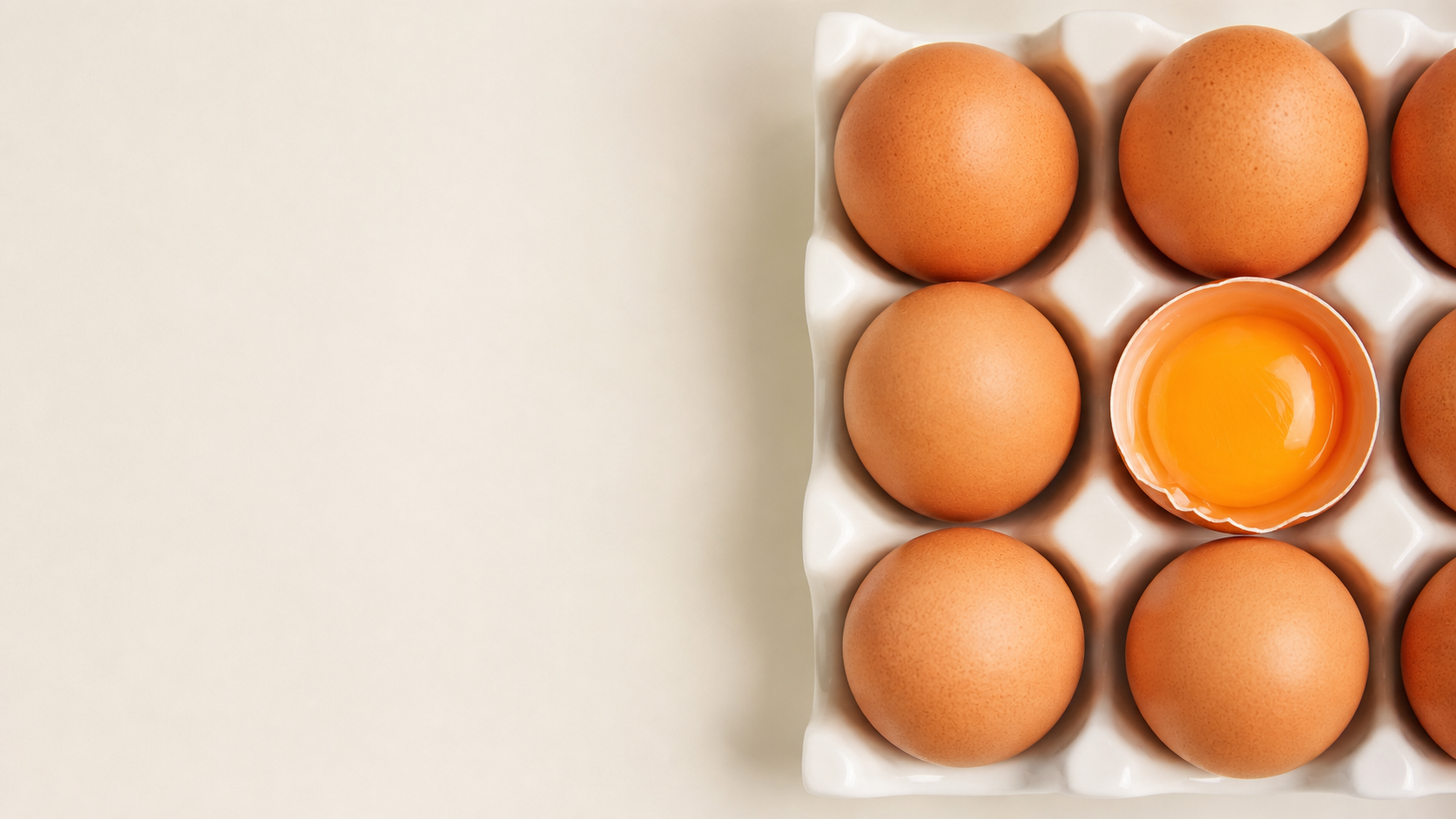 Brown eggs in a ceramic tray with one freshly cracked golden yolk